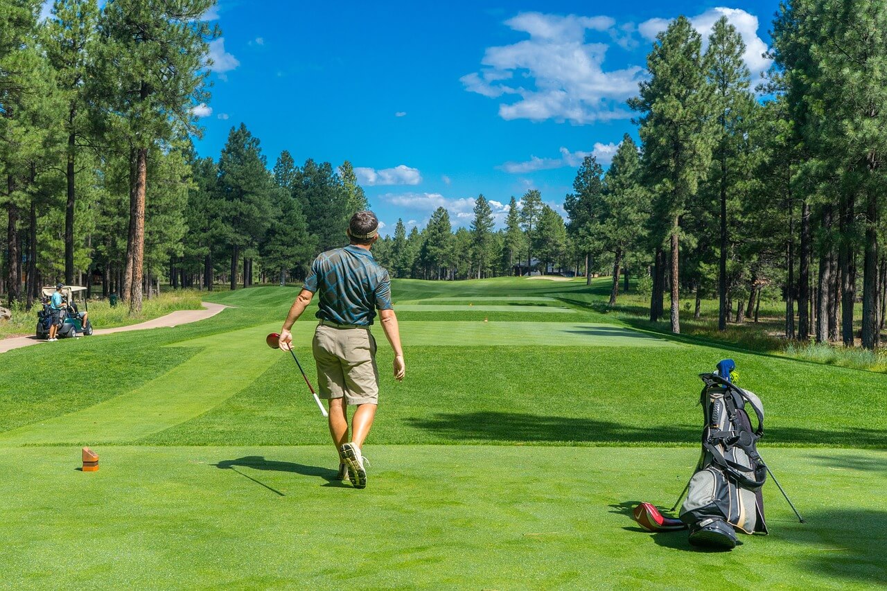 A golfer walking towards the fairway with a club in hand